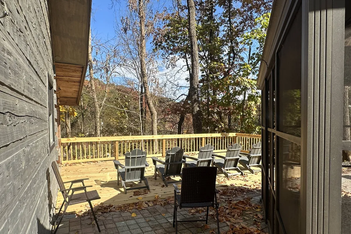 A wooden deck set with Adirondack chairs overlooks a serene forest backdrop, inviting relaxation and socialization outdoors. The setting is ideal for both day and evening gatherings, from morning coffee to stargazing at night.