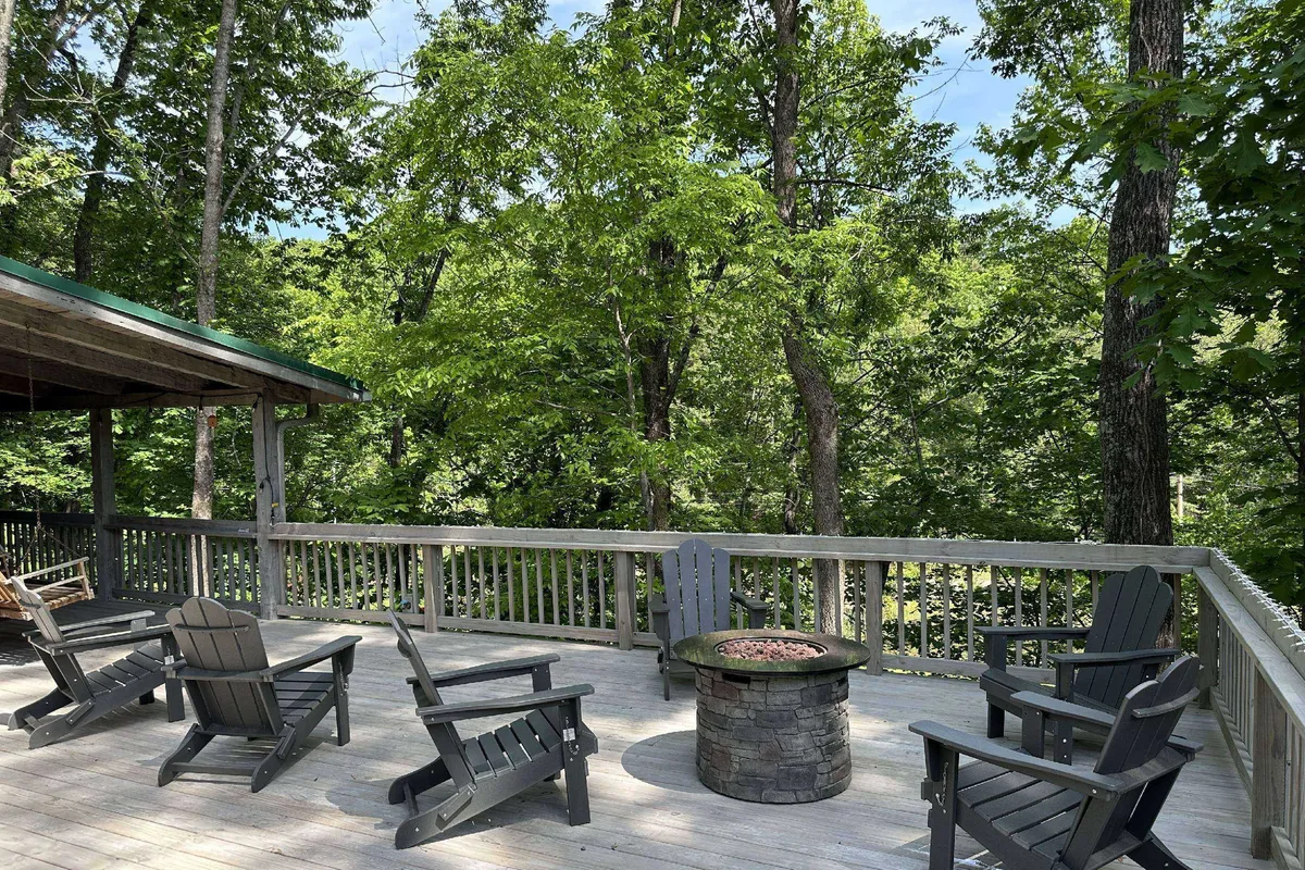 A cozy fire pit area surrounded by Adirondack chairs sits beneath leafy trees, inviting guests to gather for s’mores, storytelling, or relaxed evenings in nature. The setting is communal yet intimate, emphasizing outdoor relaxation and connection.