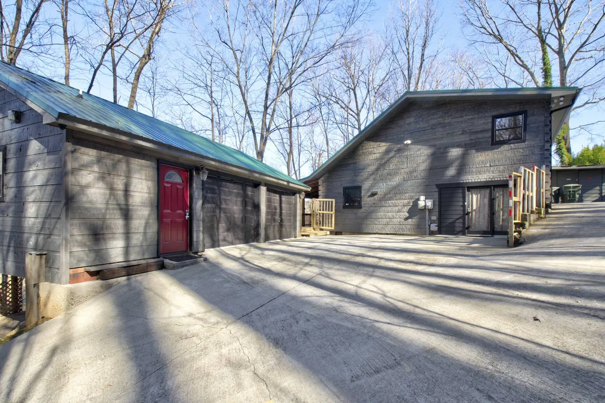A view of the cabin's red door entry, set against contrasting metal roofing and rich wooden textures. The surrounding landscape hints at peaceful nature and an inviting outdoor environment ideal for returning after city adventures.