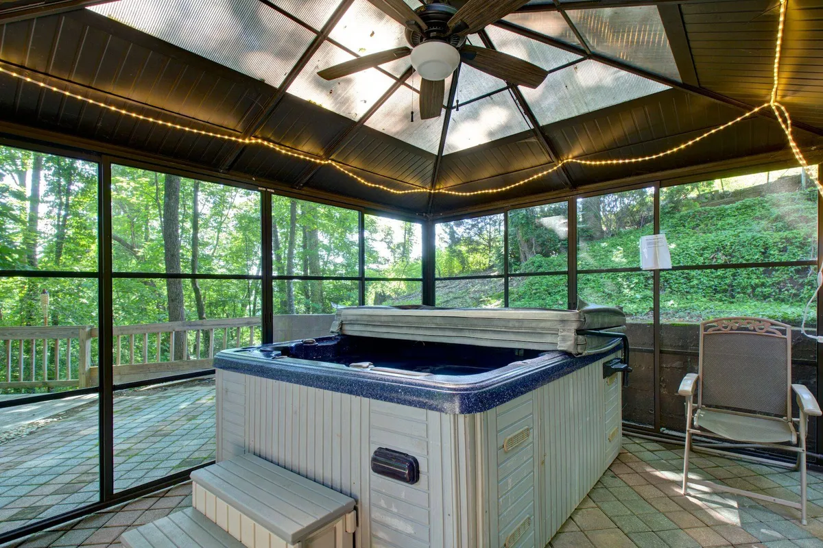 An inviting hot tub enclosed by mesh walls sits amidst greenery. String lights overhead and a ceiling fan create a cozy, all-weather atmosphere, perfect for unwinding while enjoying the sights and sounds of nature.