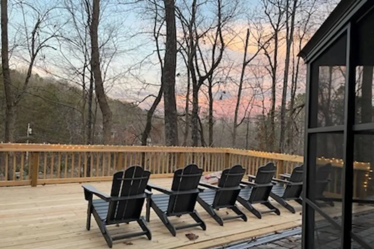 A spacious wooden deck set among trees, featuring Adirondack chairs that invite guests to relax and socialize. The scene is bathed in warm sunset light, evoking feelings of togetherness and peace within a natural setting.