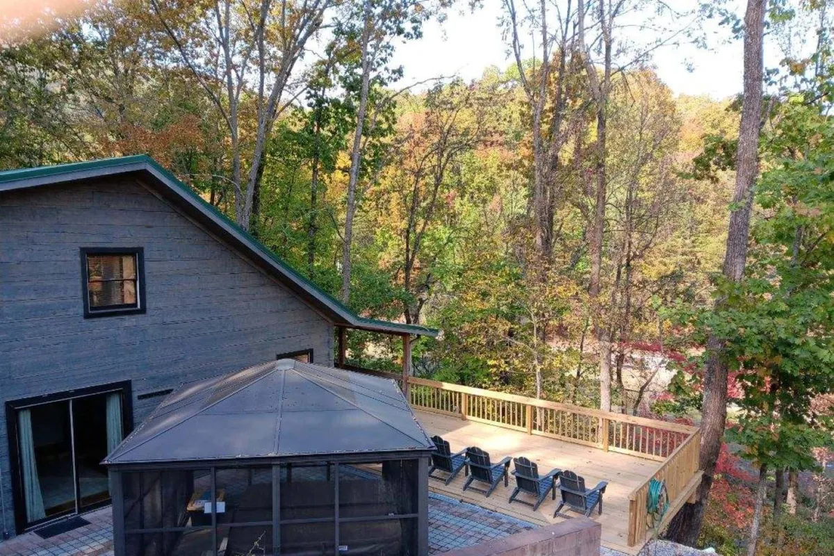 A spacious wooden deck with a screened gazebo, surrounded by lush trees and equipped with inviting lawn chairs. The scene evokes outdoor relaxation, socializing, and enjoying the serene environment after a day of sightseeing.