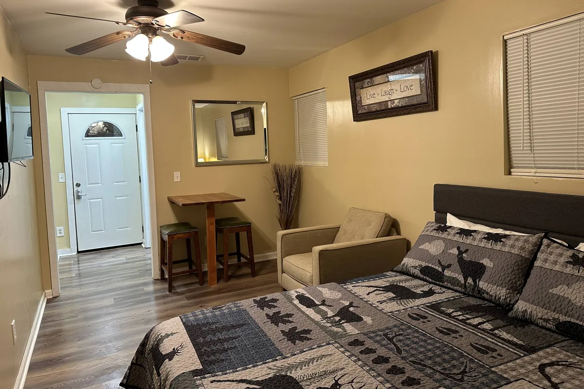 A compact but thoughtfully designed suite featuring a bed with patterned bedding, a small dining table with chairs, an entry door, and a mirror. The space feels private yet inviting, suggesting both relaxation and the ability to enjoy light meals or snacks.