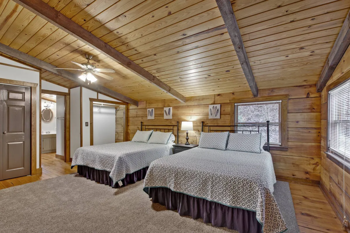 A comfortable bedroom with two double beds, a nightstand with lamp, and wooden ceiling beams. Decorative wall art adds a homey touch, making it a perfect space for siblings, cousins, or friends to share.