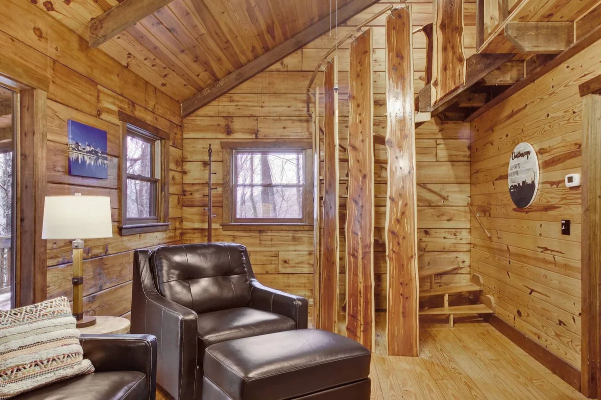 This scene presents comfortable leather chairs, a wooden staircase, and wood-paneled walls, evoking a classic cabin vibe. The arrangement invites relaxation and socialization, suggesting both casual conversation and more lively group activities like game nights.