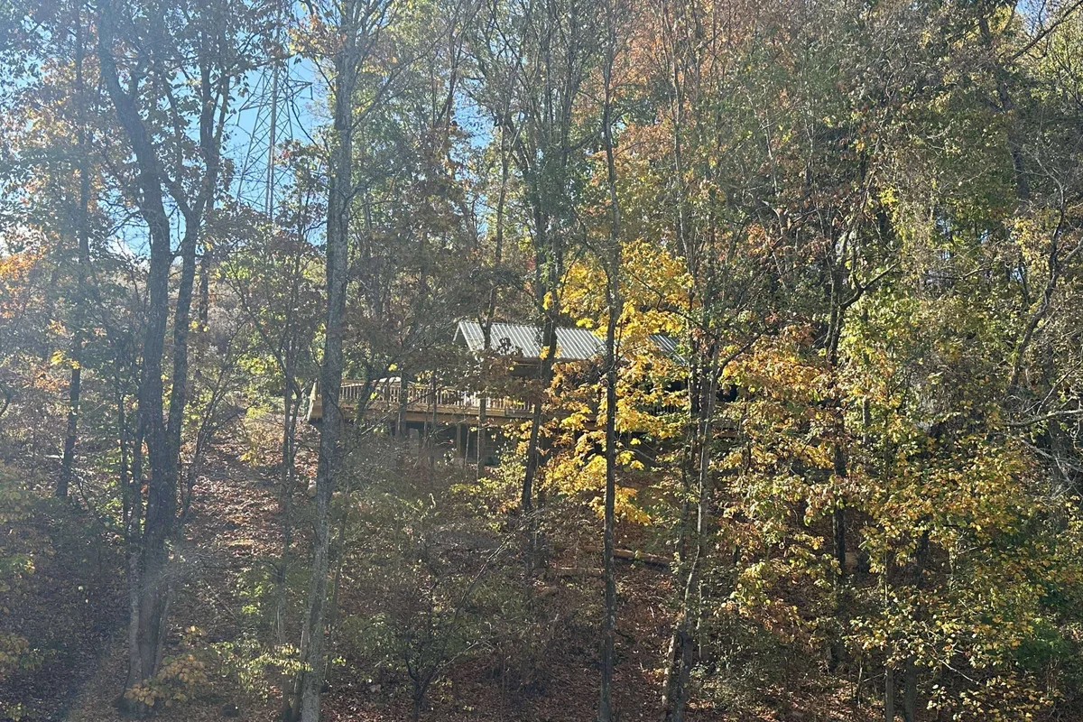 A rustic wooden cabin surrounded by vibrant autumn foliage and tall trees, set in a serene natural landscape. The view emphasizes tranquility, seclusion, and the beauty of the cabin’s setting.